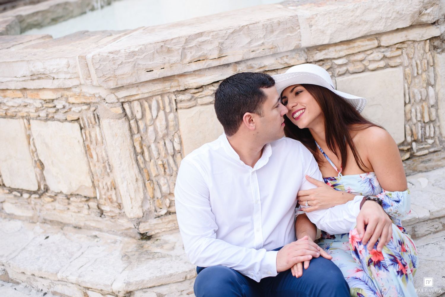 Romantic couple sharing a tender moment on ancient stone steps, woman in floral dress and white hat.