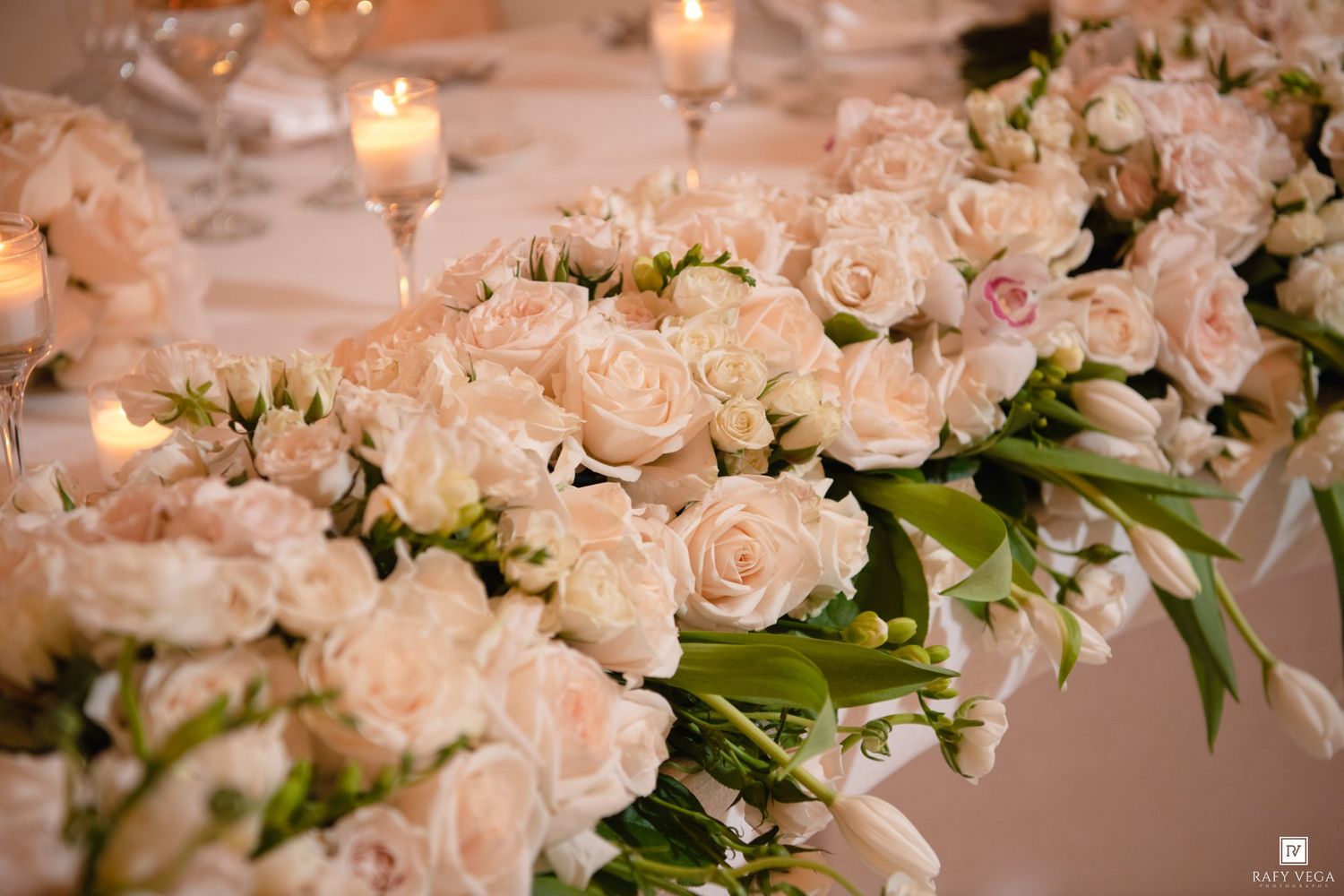 Elegant wedding centerpiece featuring lush blush pink roses and white flowers arranged with candles on a reception table.