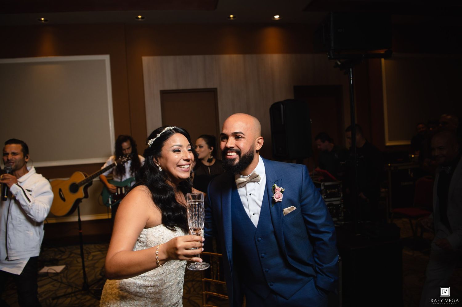 Happy bride and groom smiling together at wedding reception, groom in blue suit.