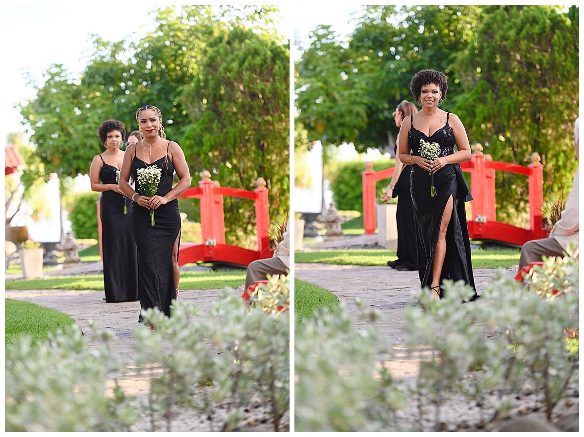 Two bridesmaids in black gowns walk through a garden venue with a red decorative arch backdrop.