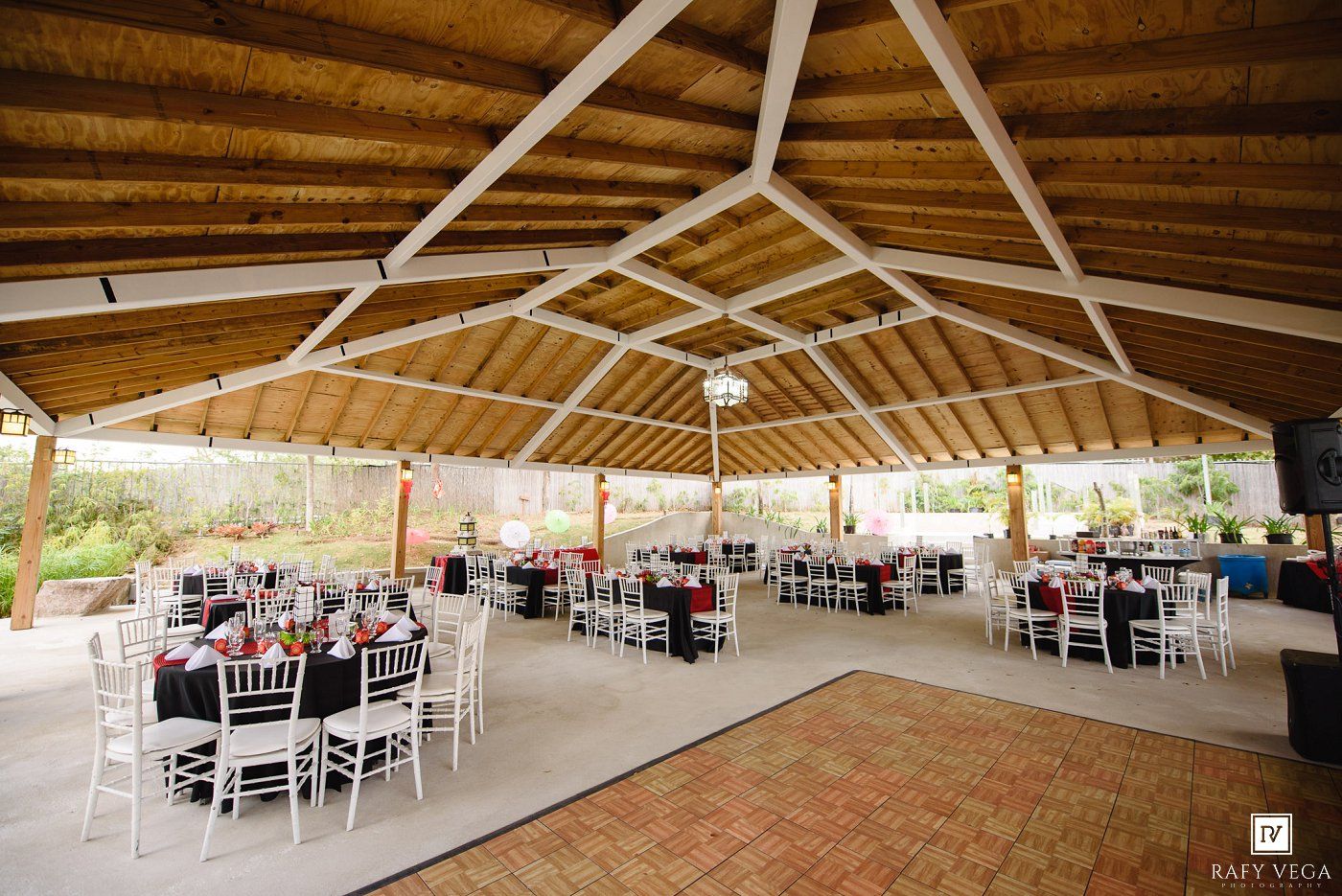 Elegant outdoor wedding reception venue with wooden roof, white chairs, and decorated tables.