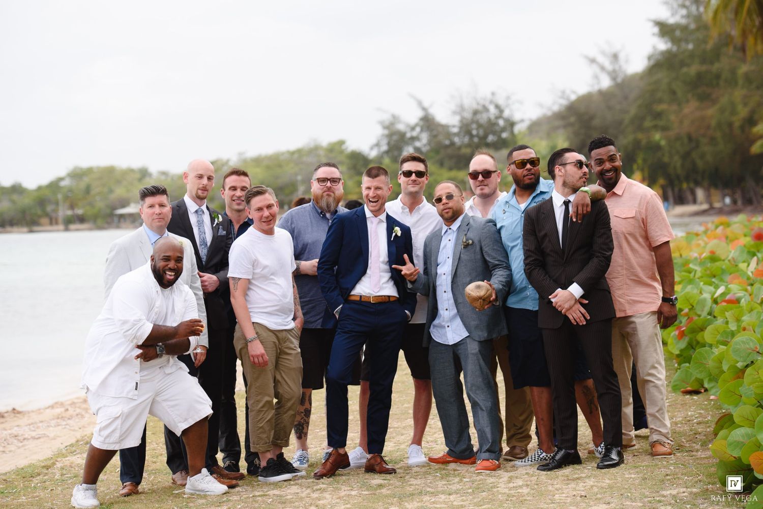 Group of well-dressed men posing together on a tropical beach for a wedding party photo.