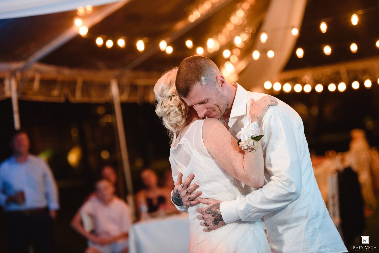 Bride and groom share an intimate first dance under warm string lights at their outdoor wedding reception.