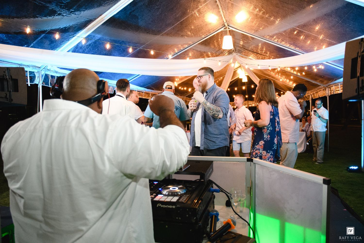 DJ performing at an outdoor wedding reception under a tent with guests dancing in the background.