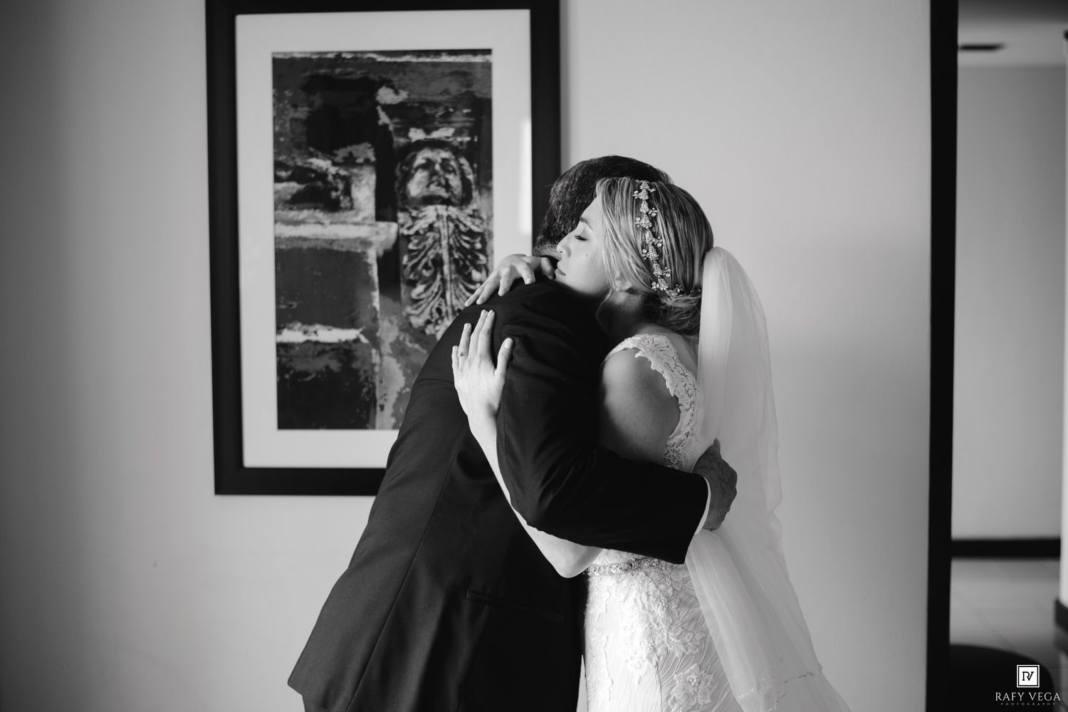 Black and white photo of a bride in a lace gown embracing someone in a suit before her wedding ceremony.