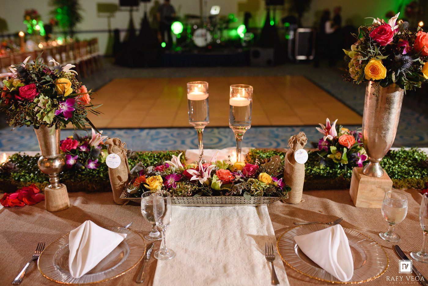 Elegant wedding reception table with colorful floral centerpieces, candles, and place settings on a burlap runner.
