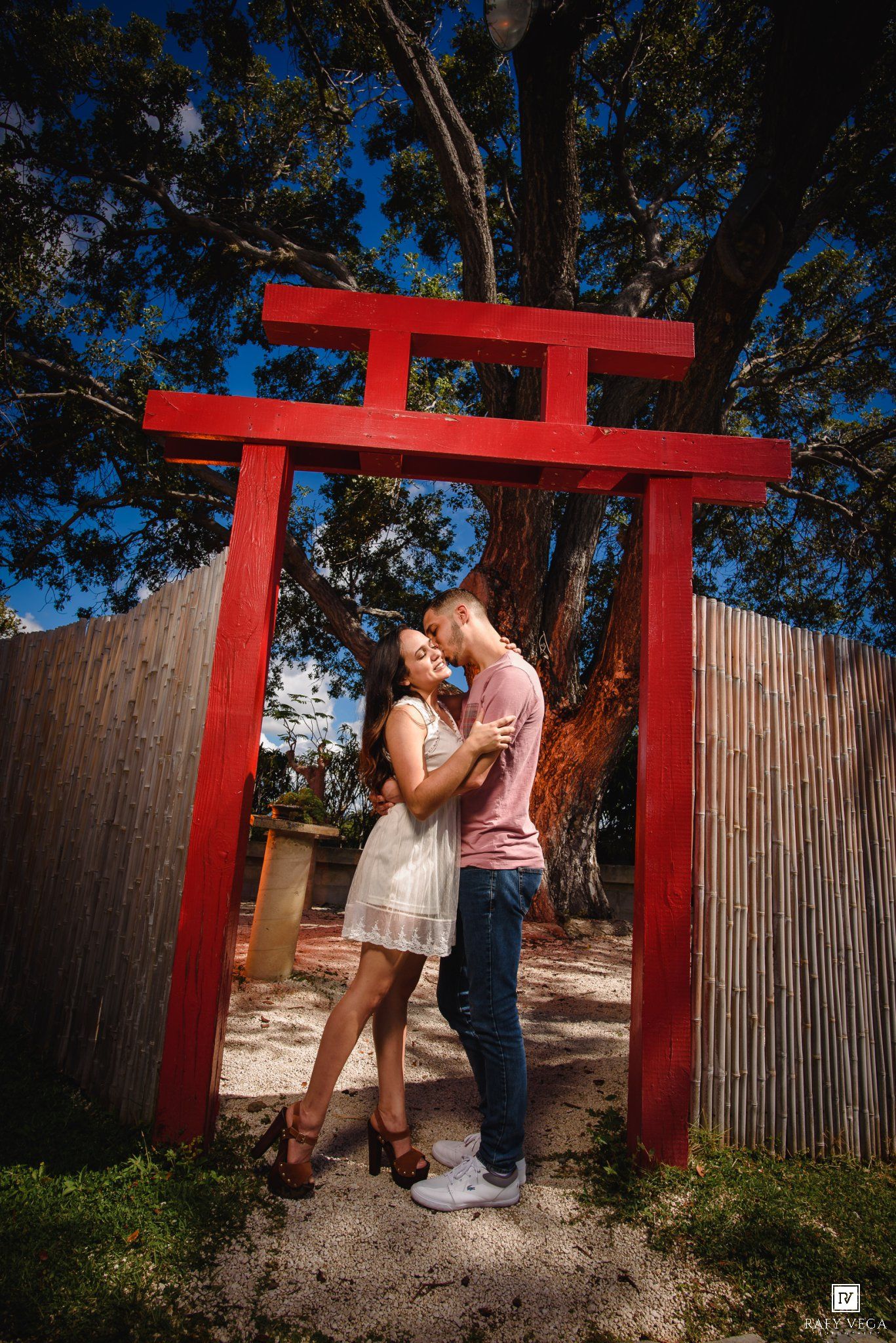 Couple sharing a romantic moment under a red Japanese torii gate surrounded by trees and bamboo fence.