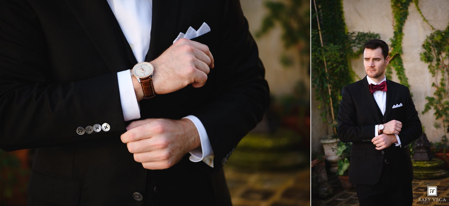 Groom in black tuxedo adjusting cufflinks and posing outdoors with bow tie and pocket square.