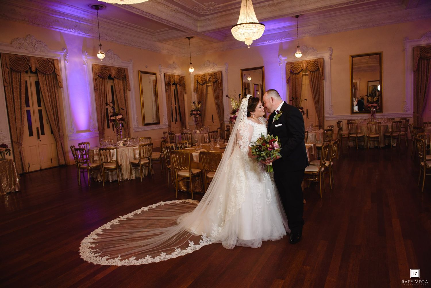 Bride and groom share a romantic kiss on the dance floor of an elegant ballroom with purple uplighting.