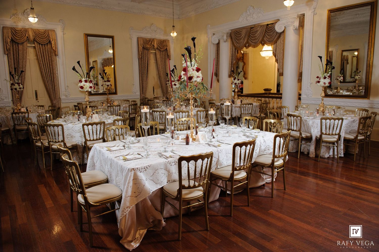 Elegant banquet hall with gold Chiavari chairs, white linen tables, floral centerpieces, and ornate decor for a wedding reception.