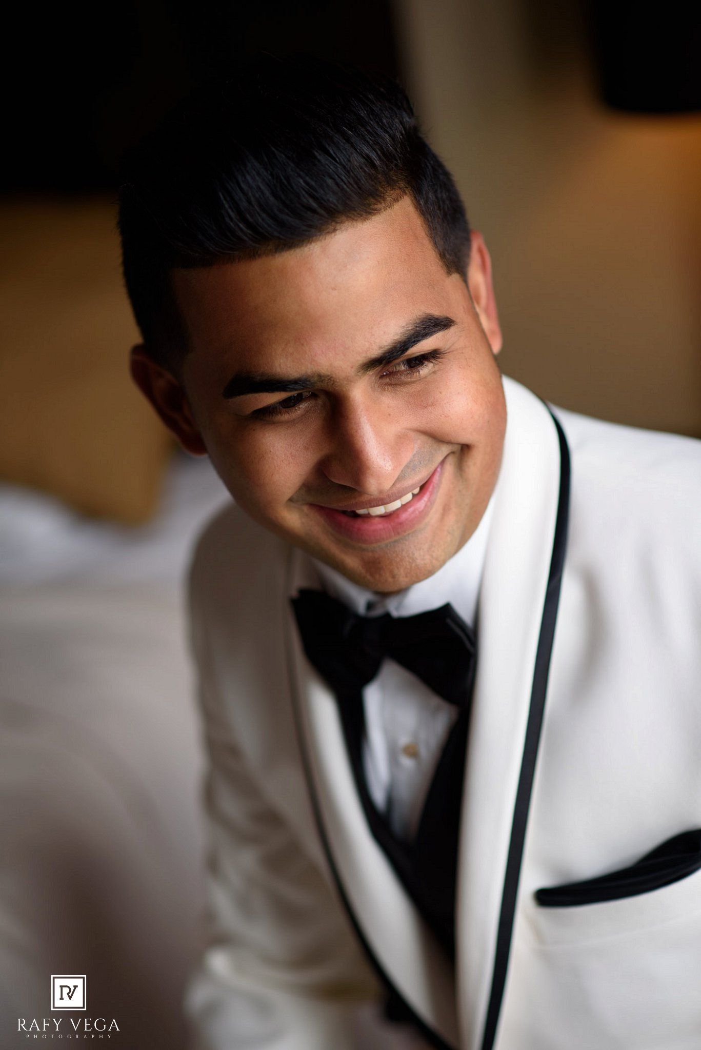 Smiling young man in white tuxedo with black bow tie and trim, photographed by Rafy Vega Photography.