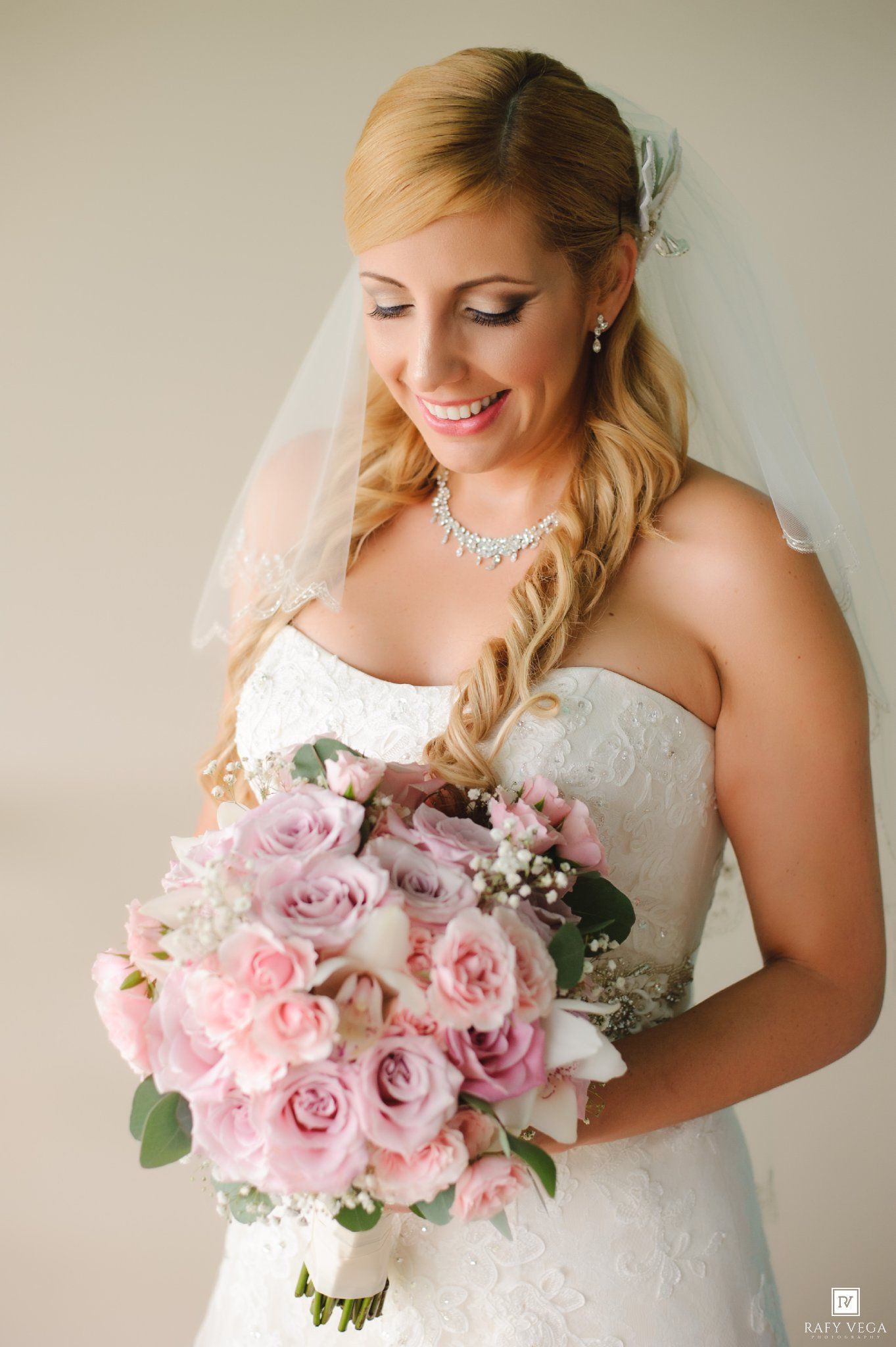 Radiant bride in strapless lace gown holding a lush pink rose bouquet with baby's breath and eucalyptus leaves.