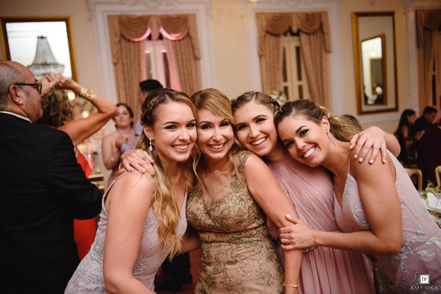 Four smiling women pose together at an elegant wedding reception in a beautifully decorated ballroom.