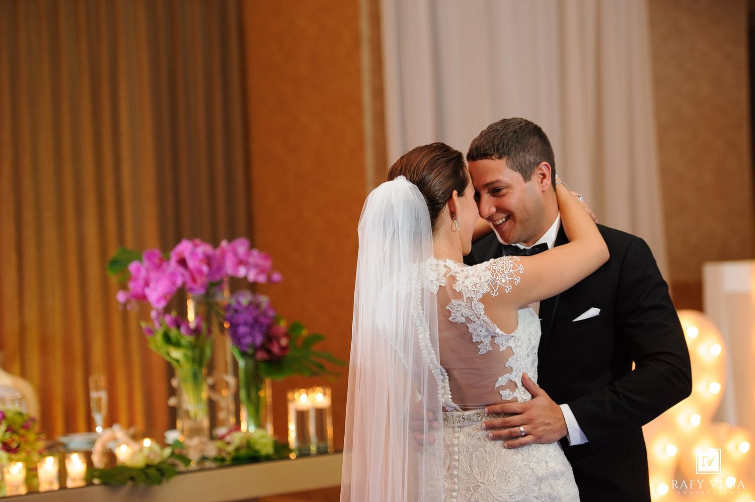 Bride and groom share an intimate moment during their first dance at elegant wedding reception with floral arrangements.