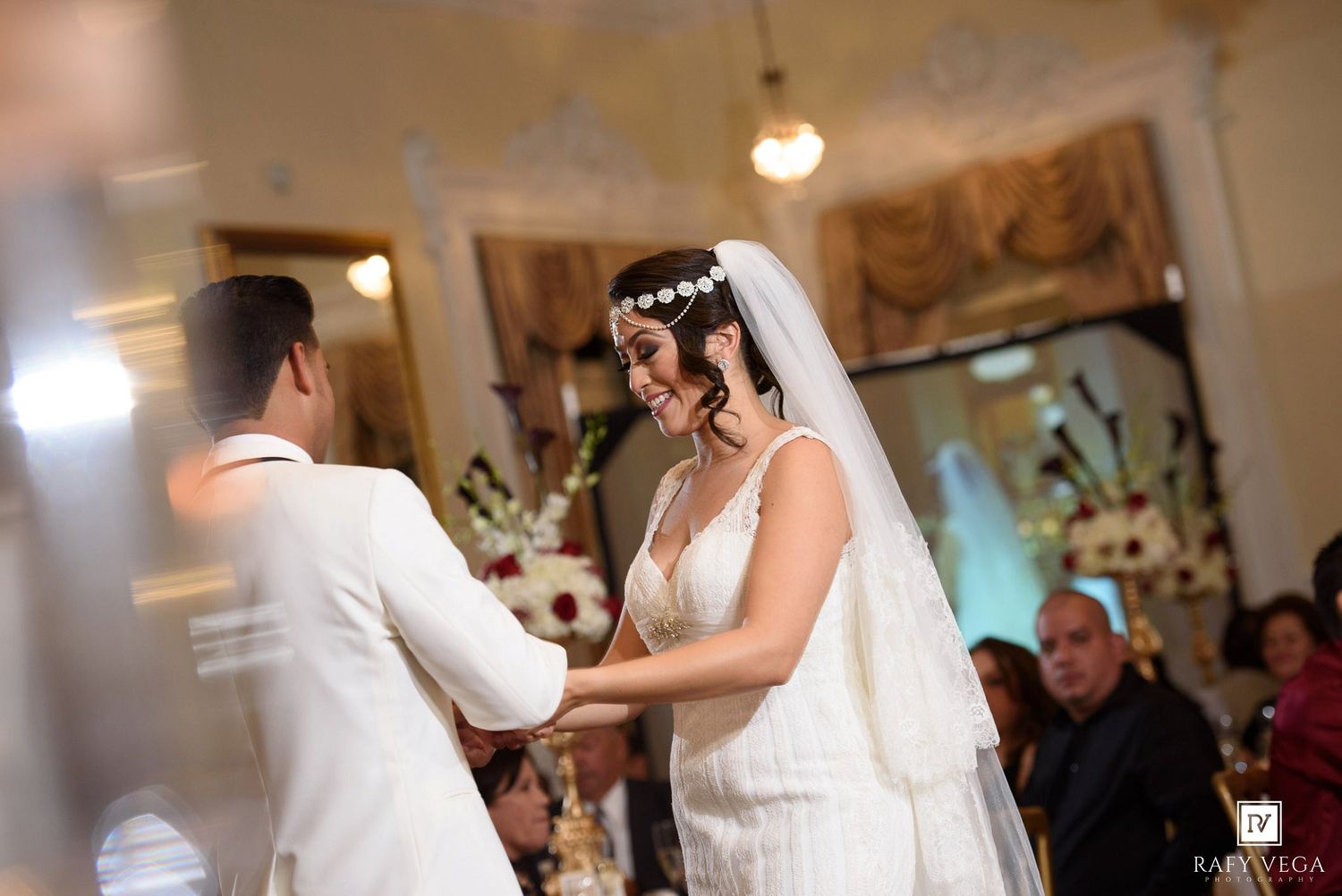 Bride and groom holding hands and smiling during elegant indoor wedding ceremony.