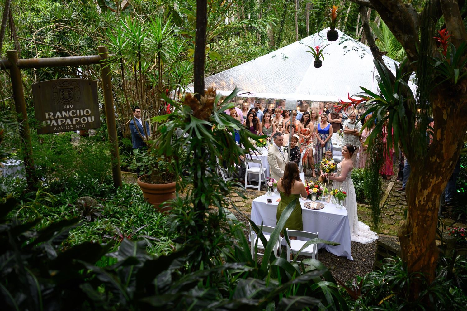 Outdoor wedding ceremony at Rancho Papapos, surrounded by lush tropical greenery with guests seated under a white tent.
