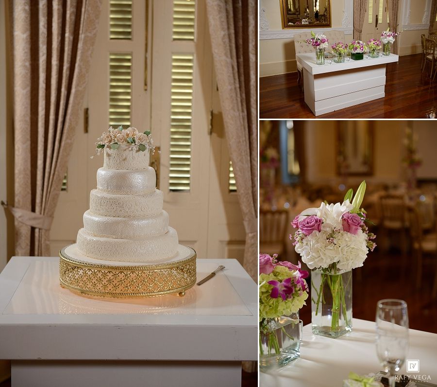 Elegant four-tier white wedding cake on gold stand with floral topper, reception table florals, and white buffet table decor.