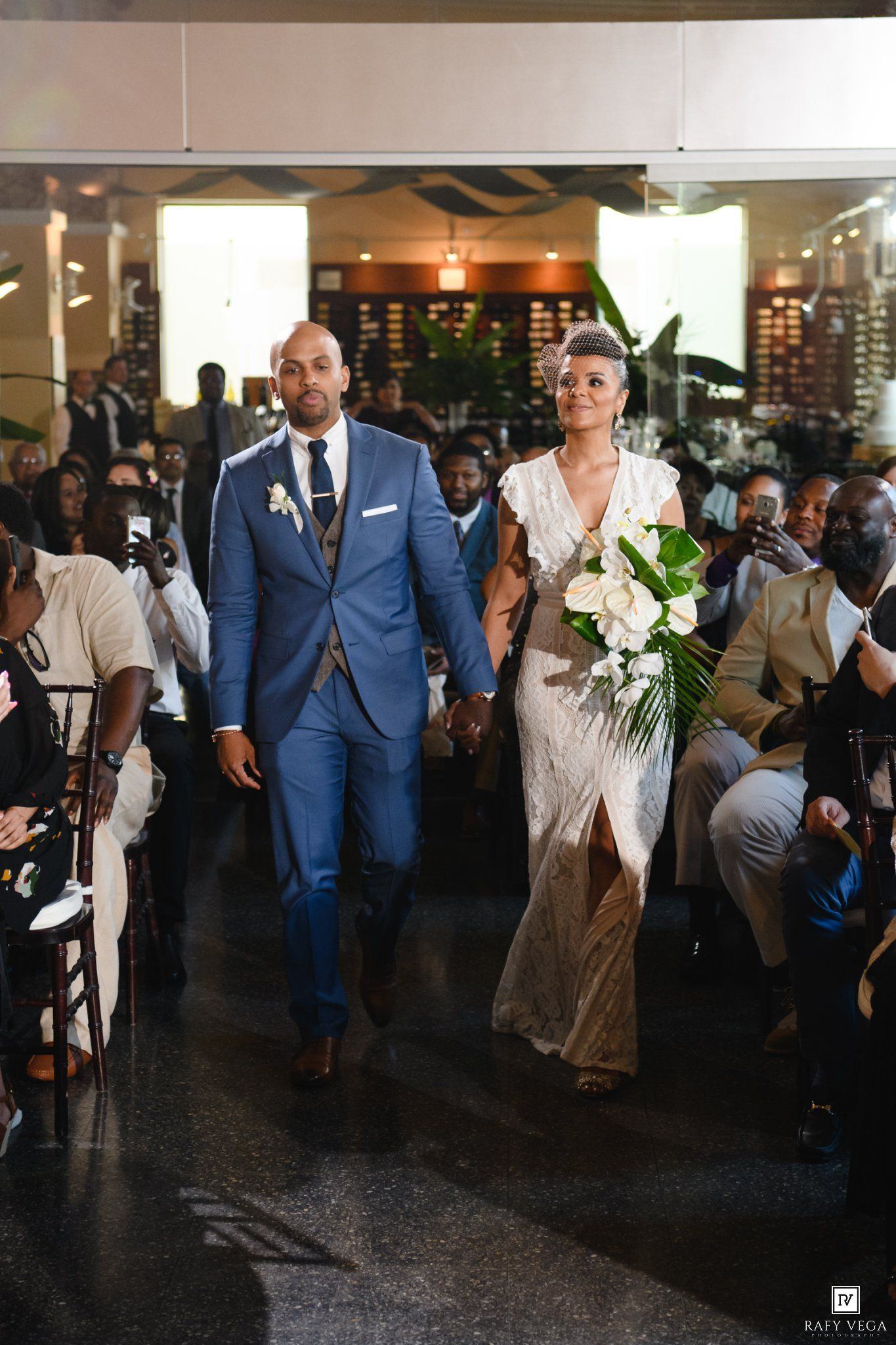 Bride and groom walk hand-in-hand down the aisle at their elegant indoor wedding ceremony.