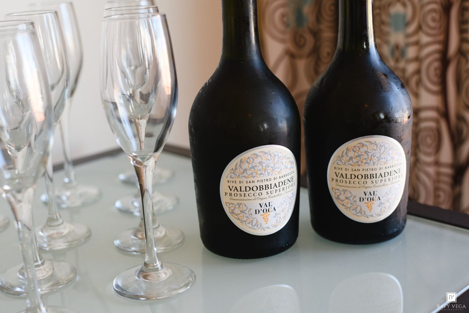Two bottles of Valdobbiadene Prosecco beside elegant champagne flutes on a glass table.