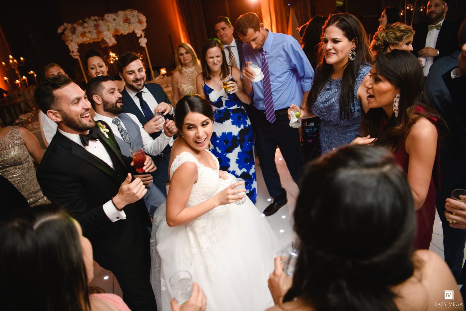 Bride in white gown dancing joyfully with groom and guests at elegant wedding reception celebration.