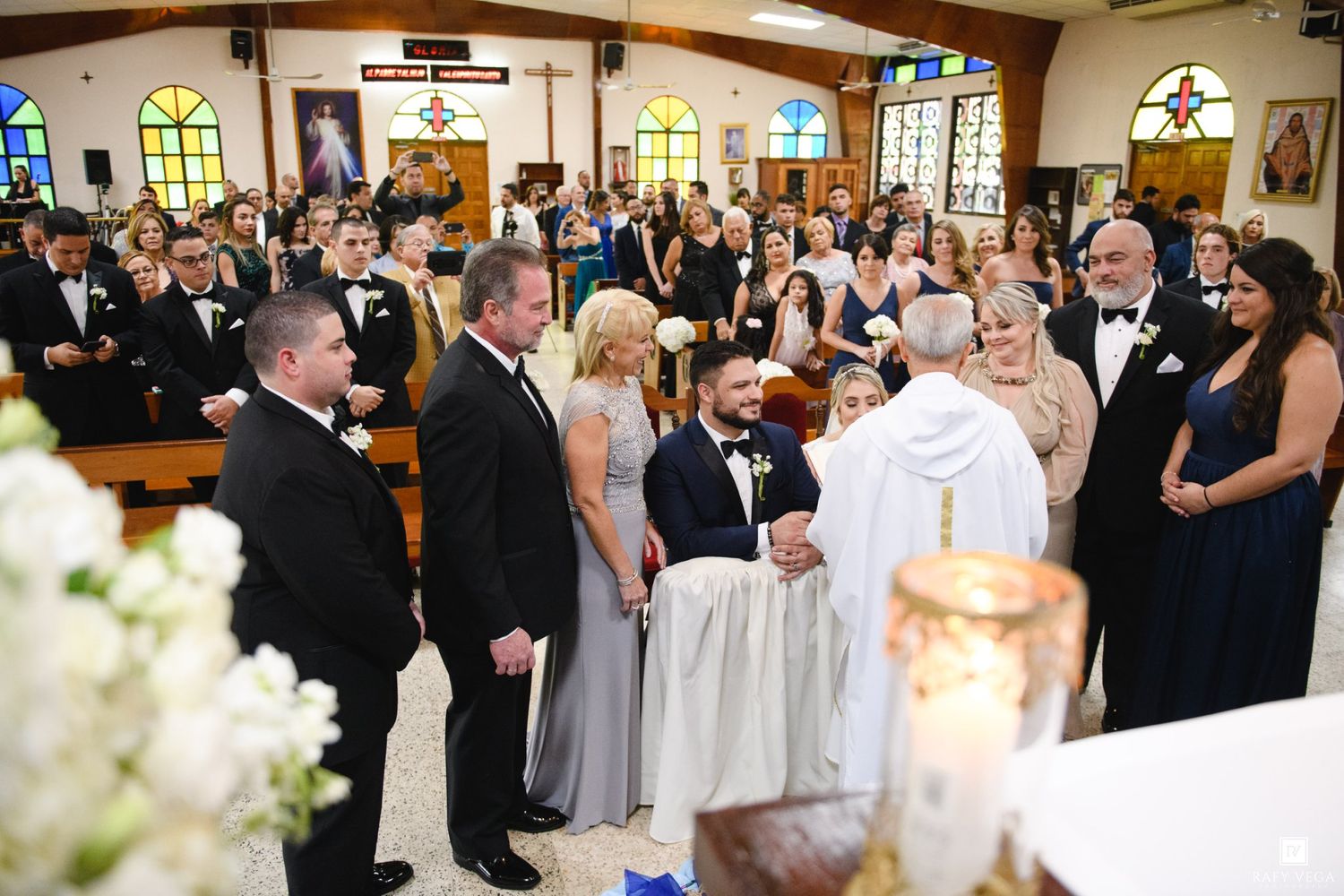 Elegant Catholic church wedding ceremony with bride and groom at altar surrounded by guests in formal attire.