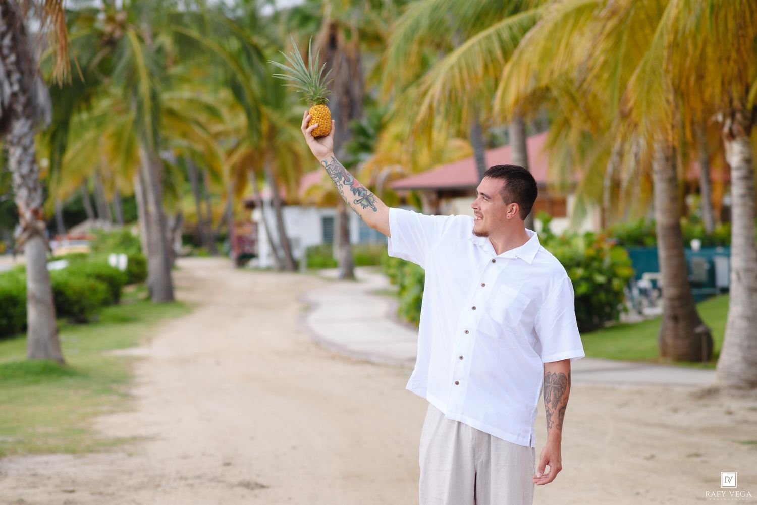 Man in white shirt holding a coconut among tropical palm trees at a Caribbean beach resort.