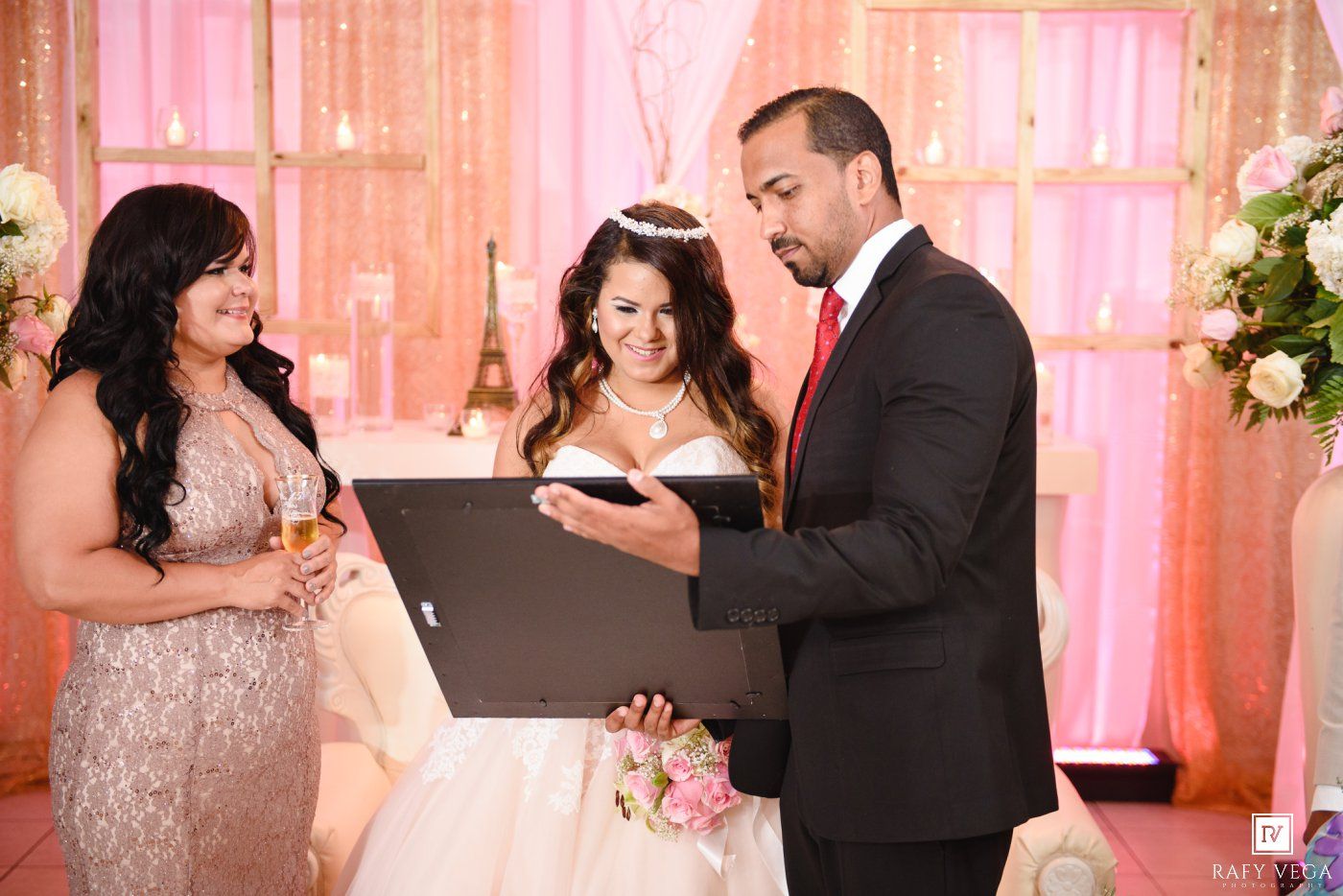Man in black suit reads from book during quinceañera ceremony beside girl in white gown.