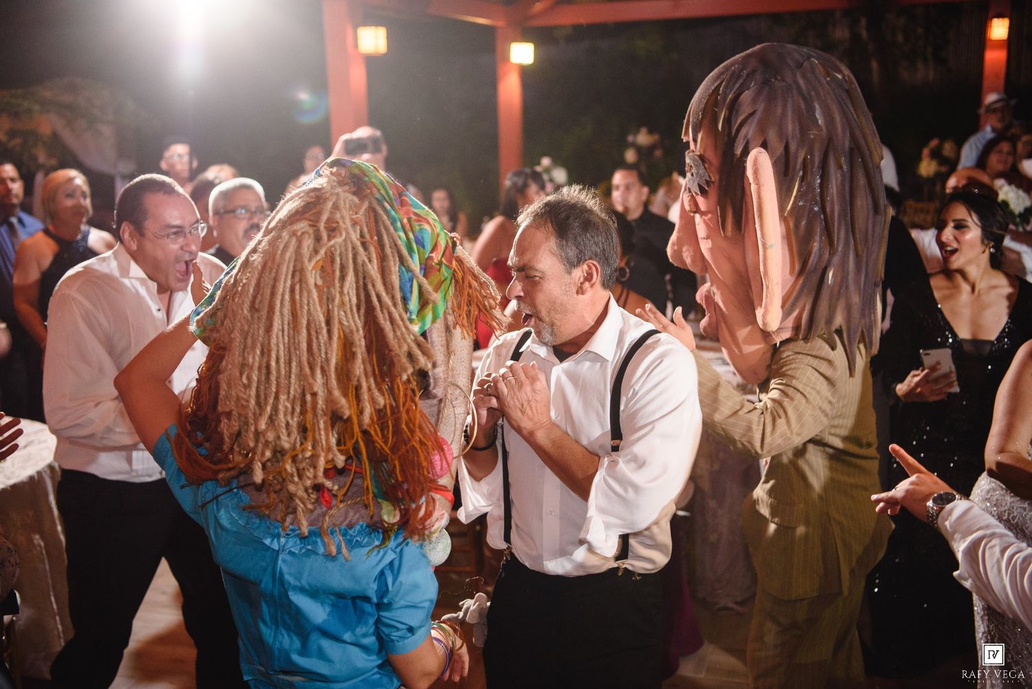 Guests dancing with large costume heads at a lively wedding reception party indoors.