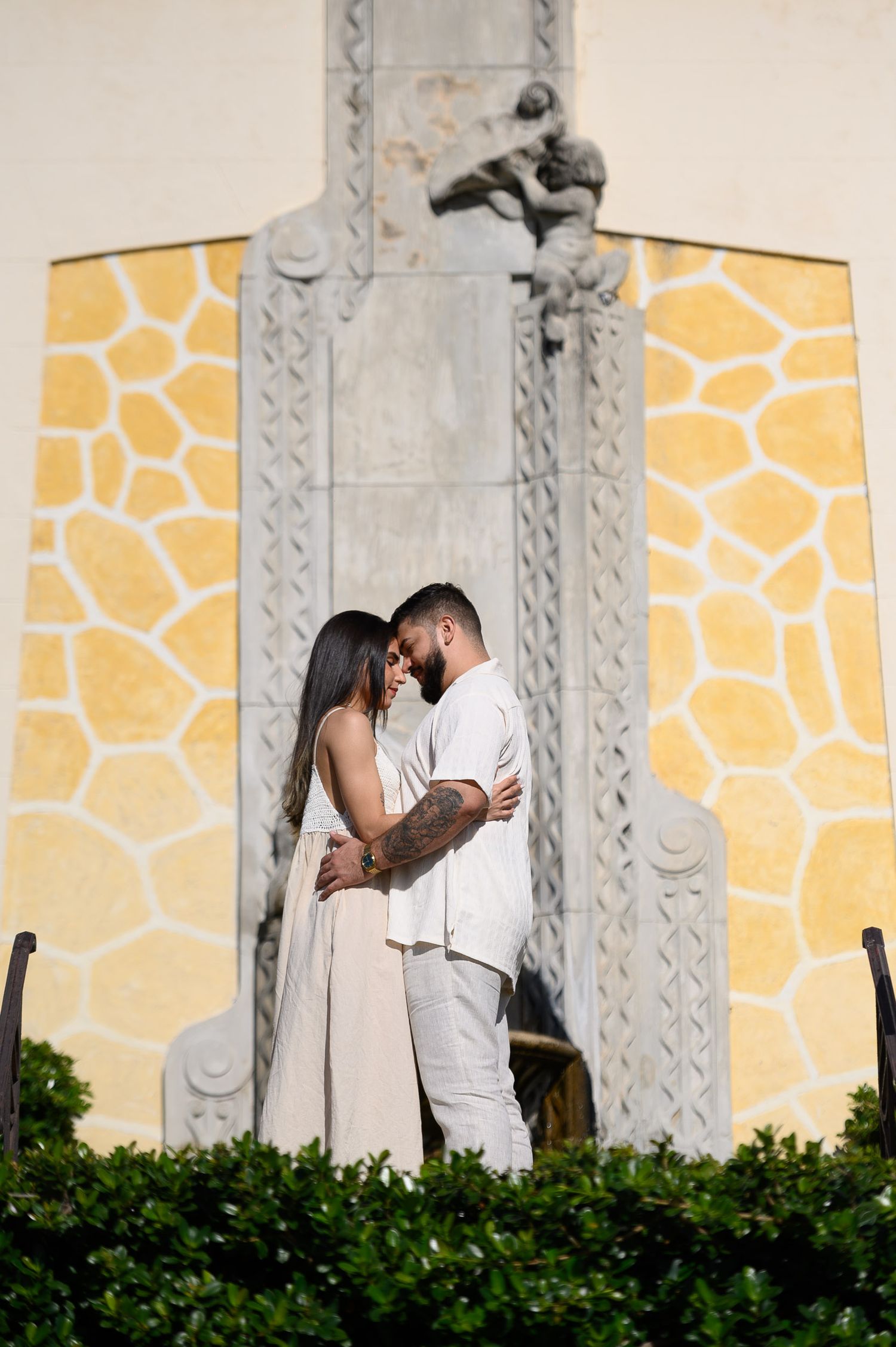 Romantic couple embracing in front of an ornate yellow stone architectural monument outdoors.