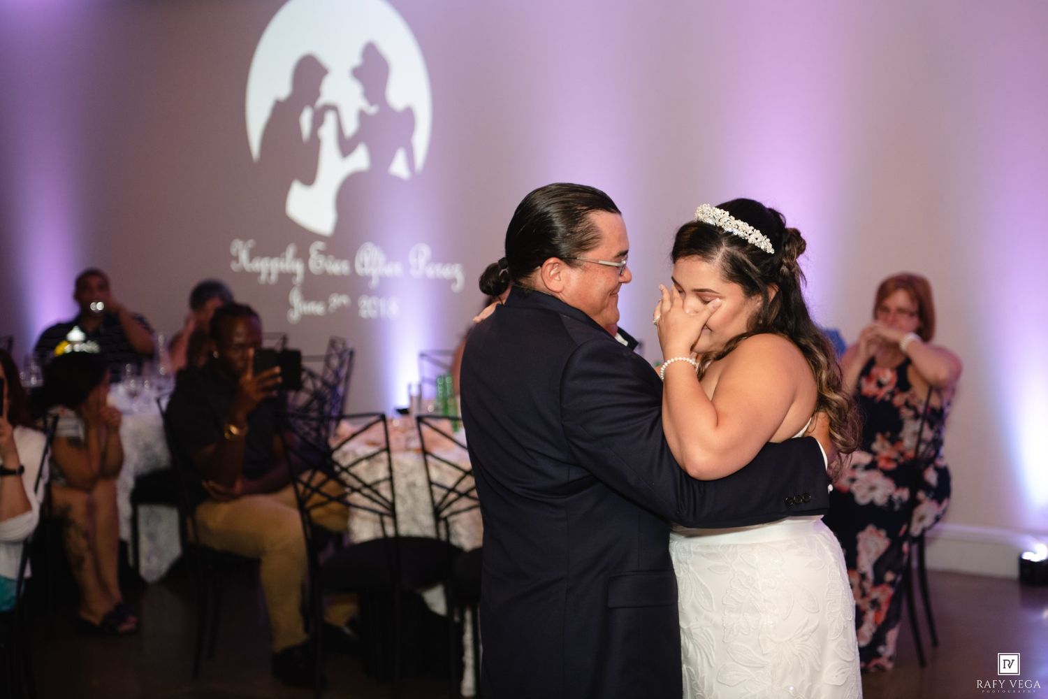 Bride and groom share an emotional first dance at their wedding reception with a romantic purple lit backdrop.