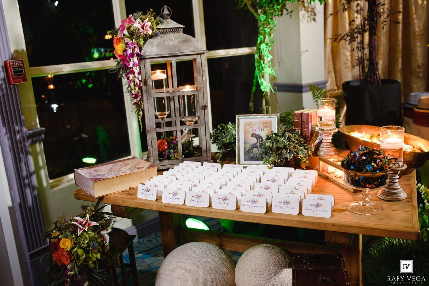 Elegant wedding escort card table with lantern, candles, floral arrangements, and neatly arranged place cards.