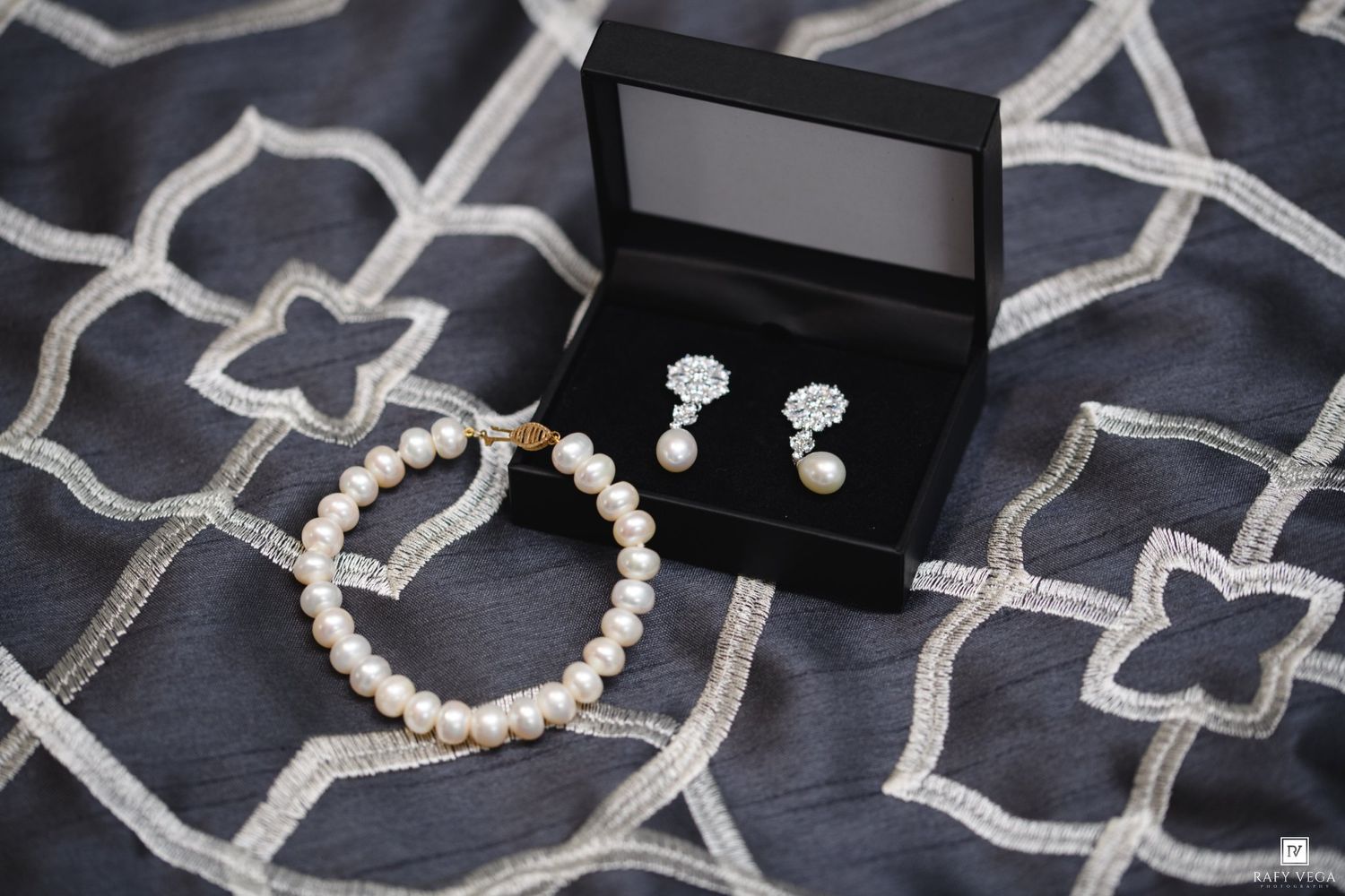 Pearl bracelet and drop earrings with crystal accents displayed in a black jewelry box on gray fabric.