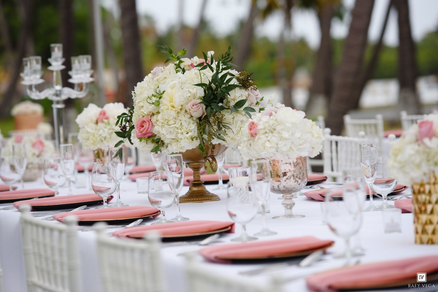 Elegant wedding reception table with white and pink floral centerpiece, crystal glasses, and coral napkins.