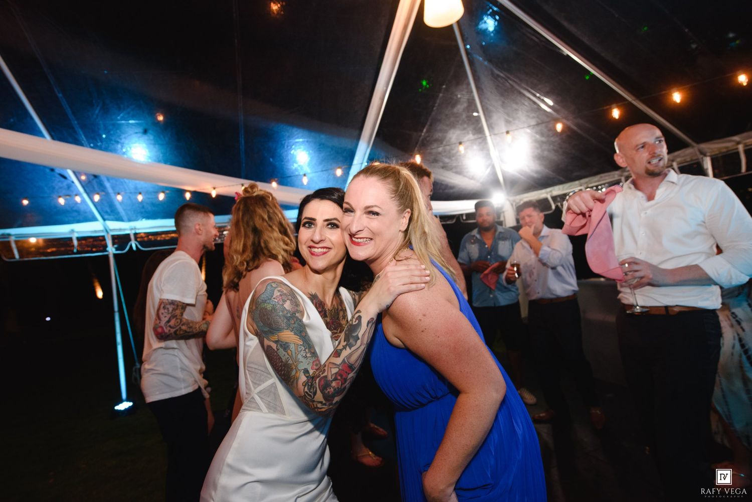 Two women smiling and posing together on the dance floor at a festive outdoor wedding reception.