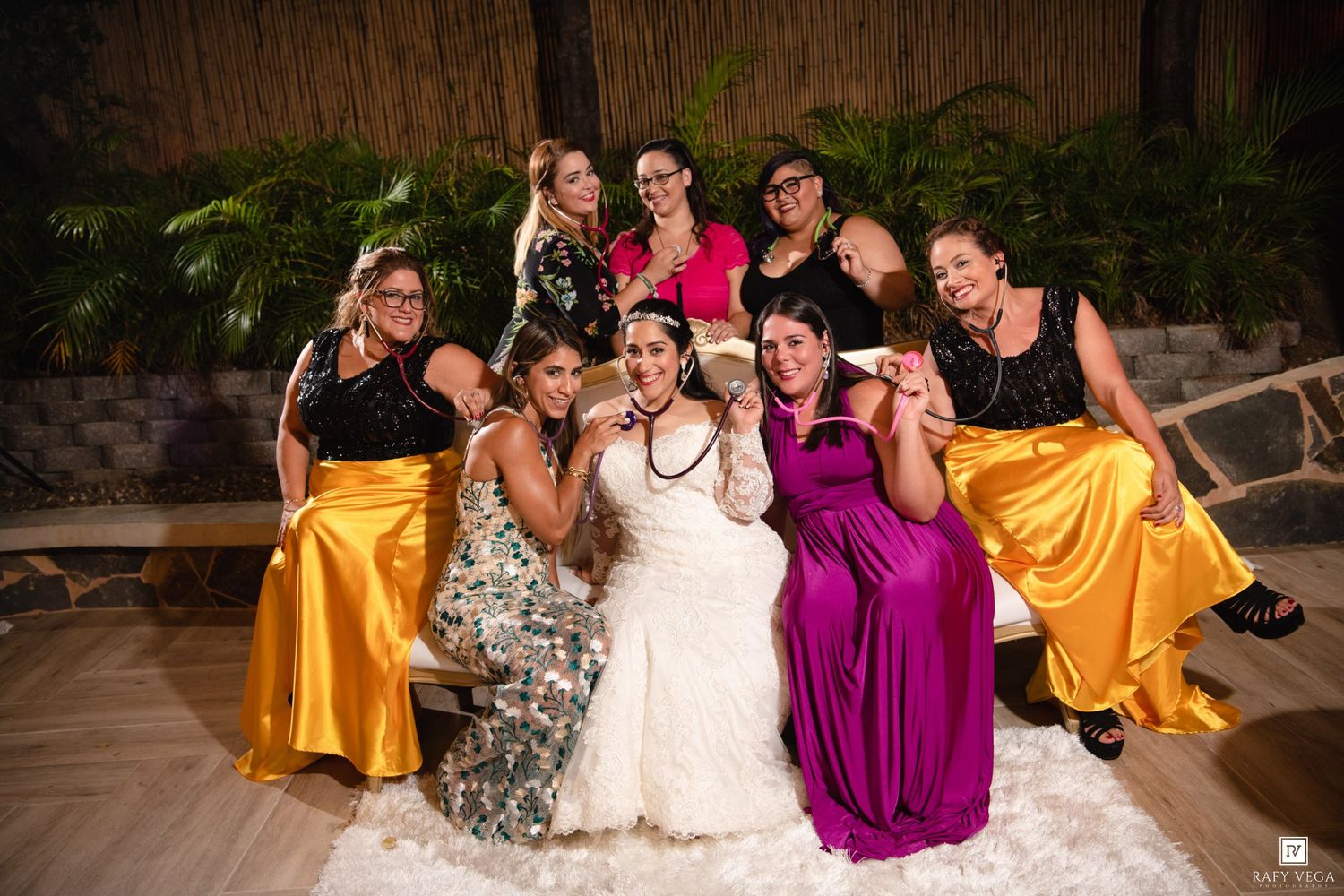Bride in white gown poses with bridesmaids in gold and pink dresses at a tropical wedding reception.