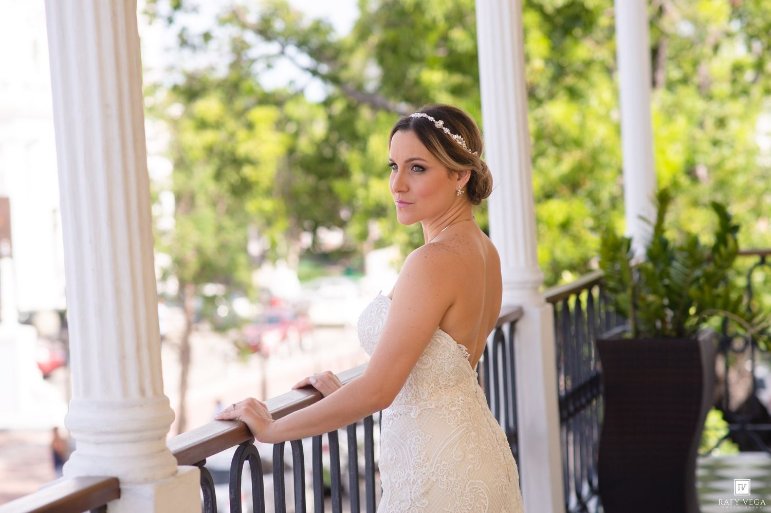 Elegant bride in a lace wedding gown posing on a white columned porch, looking over her shoulder.