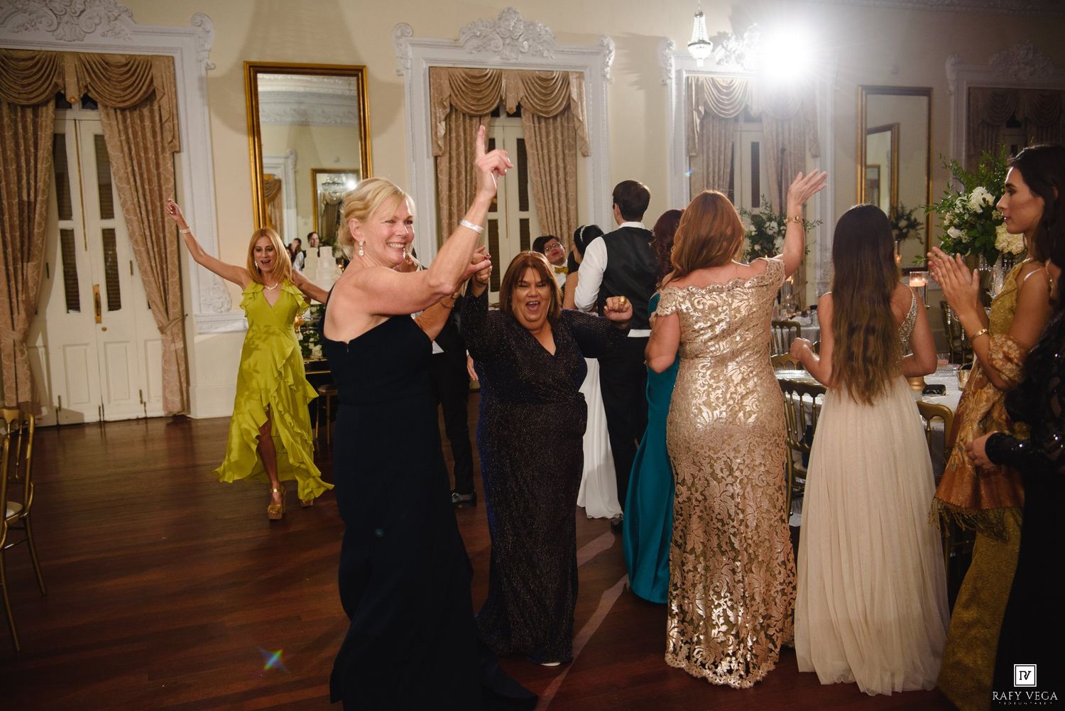Guests celebrate on the dance floor at a glamorous wedding reception in a grand venue.