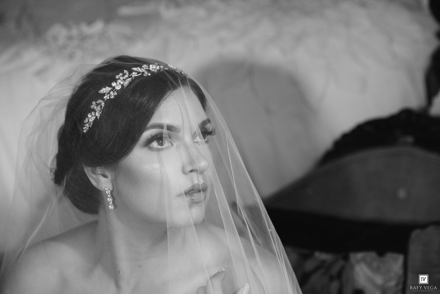 Black and white portrait of a bride wearing a veil and tiara, gazing upward with elegant earrings.