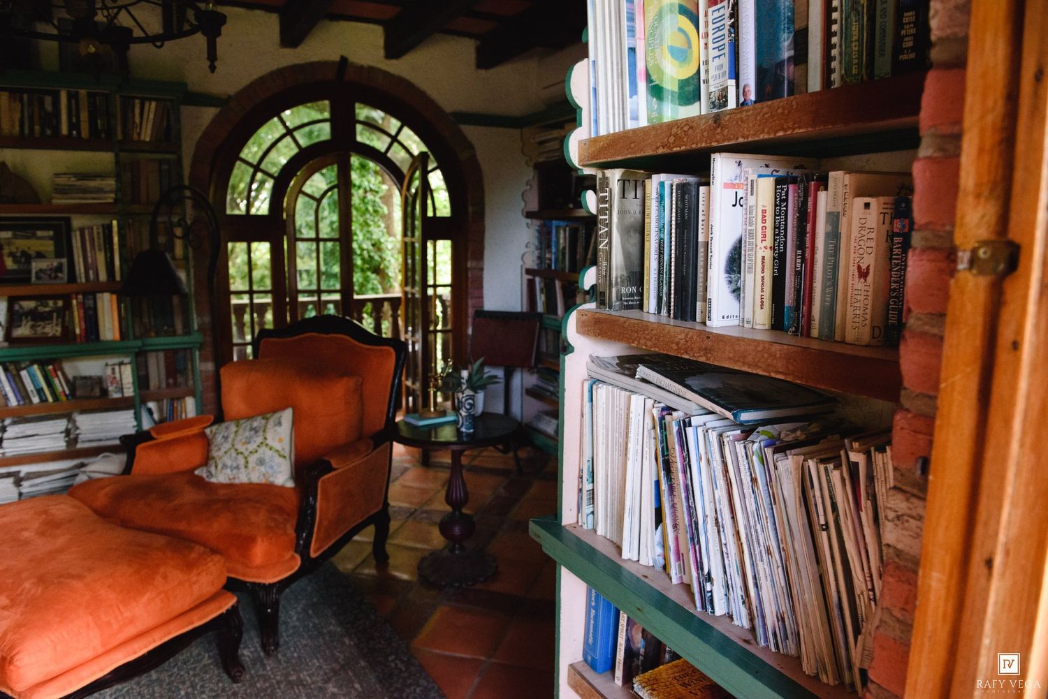 Cozy library reading nook with orange armchair, arched window, and wooden bookshelves filled with books.