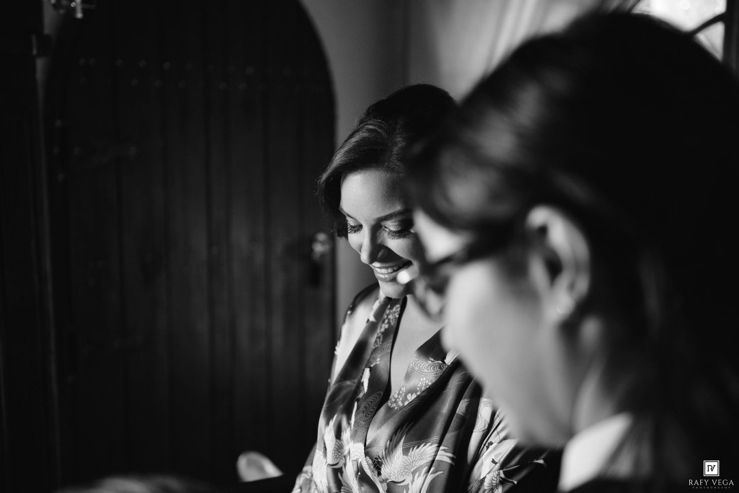 Black and white photo of two women smiling and laughing together at a wedding preparation event.
