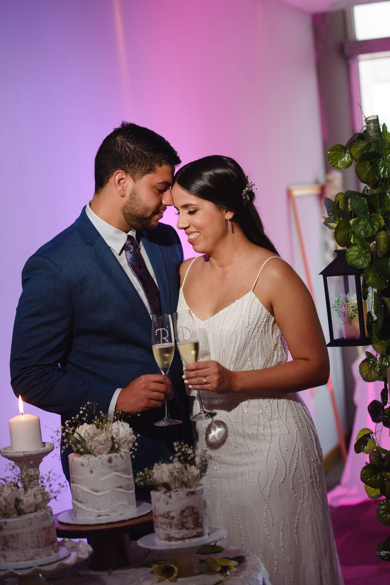 Bride and groom share a romantic moment with champagne glasses beside a wedding cake at their reception.