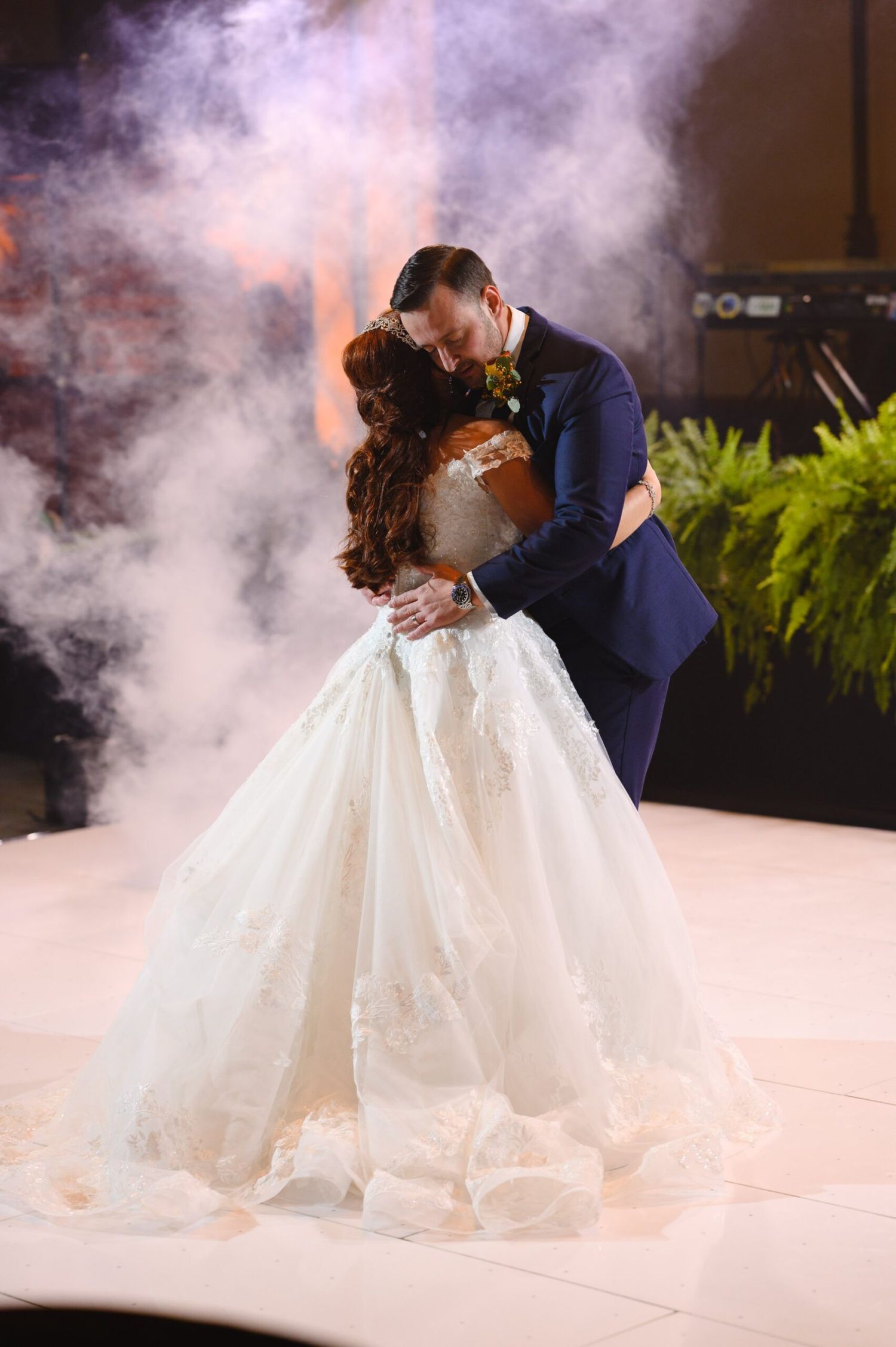 Bride and groom share a romantic first dance kiss in a cloud of fog, bride wearing a stunning ballgown.