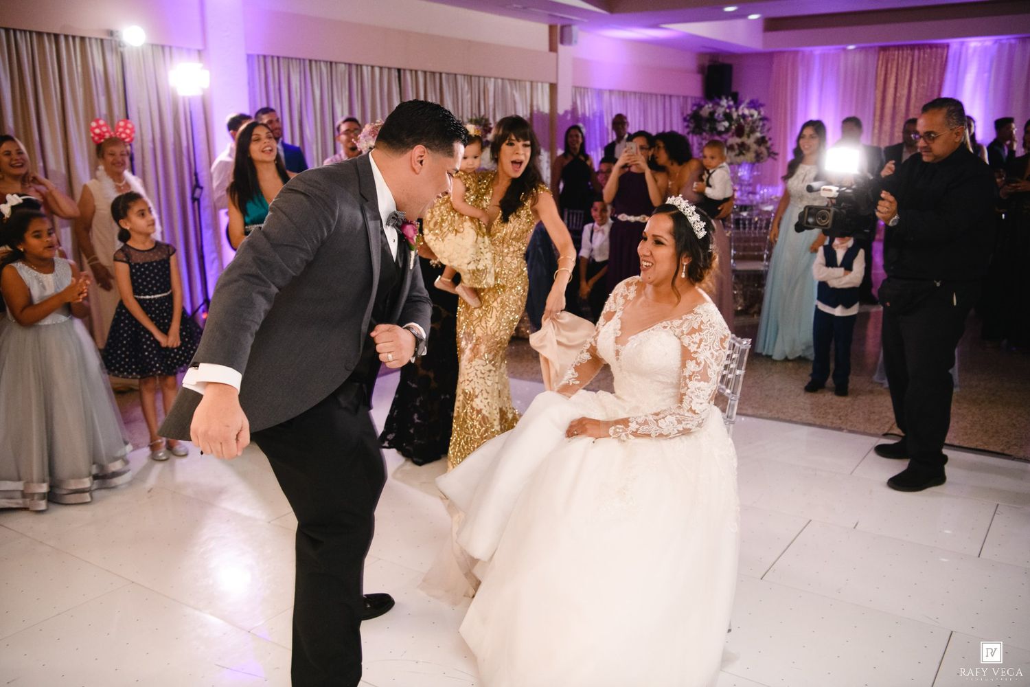 Bride and groom share playful dance moment with guests at elegant wedding reception on white dance floor.