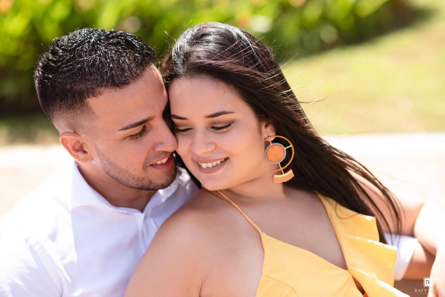 Romantic couple sharing a tender moment outdoors, woman in yellow dress with gold earrings smiling softly.