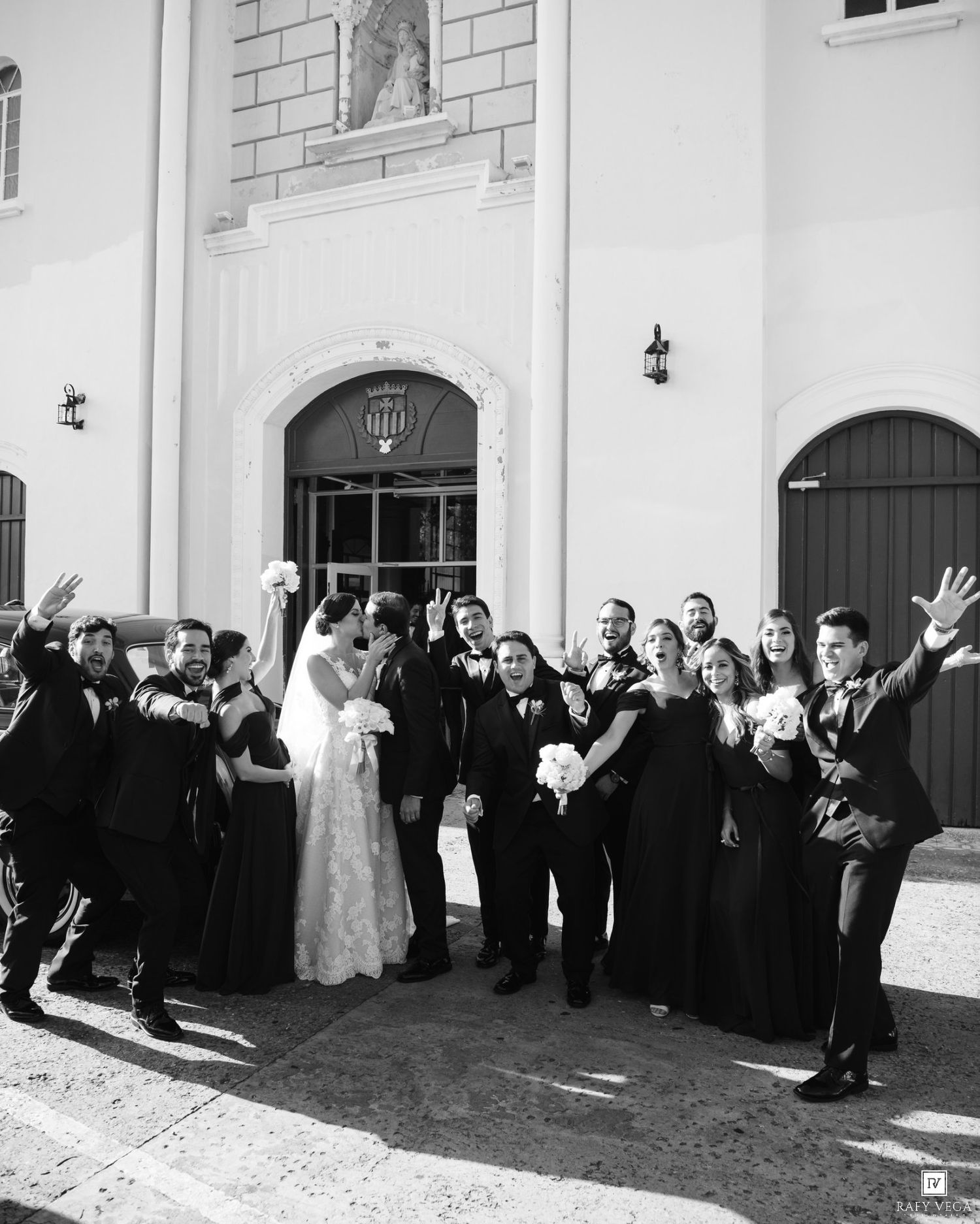 Black and white photo of a joyful wedding party celebrating outside a church.