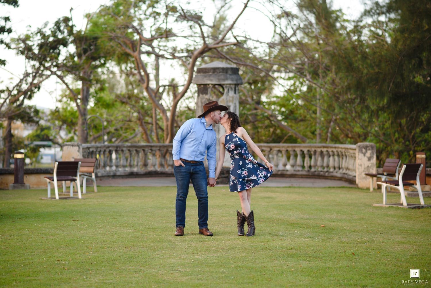 Couple sharing a romantic moment on green lawn with stone balustrade and trees in background at outdoor park.