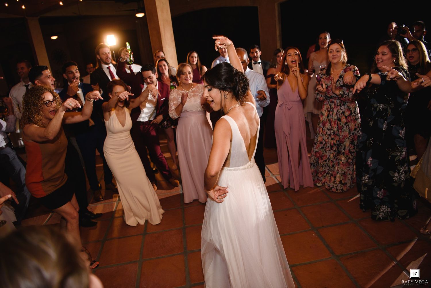 Bride twirls joyfully on the dance floor surrounded by cheering wedding guests at the reception.