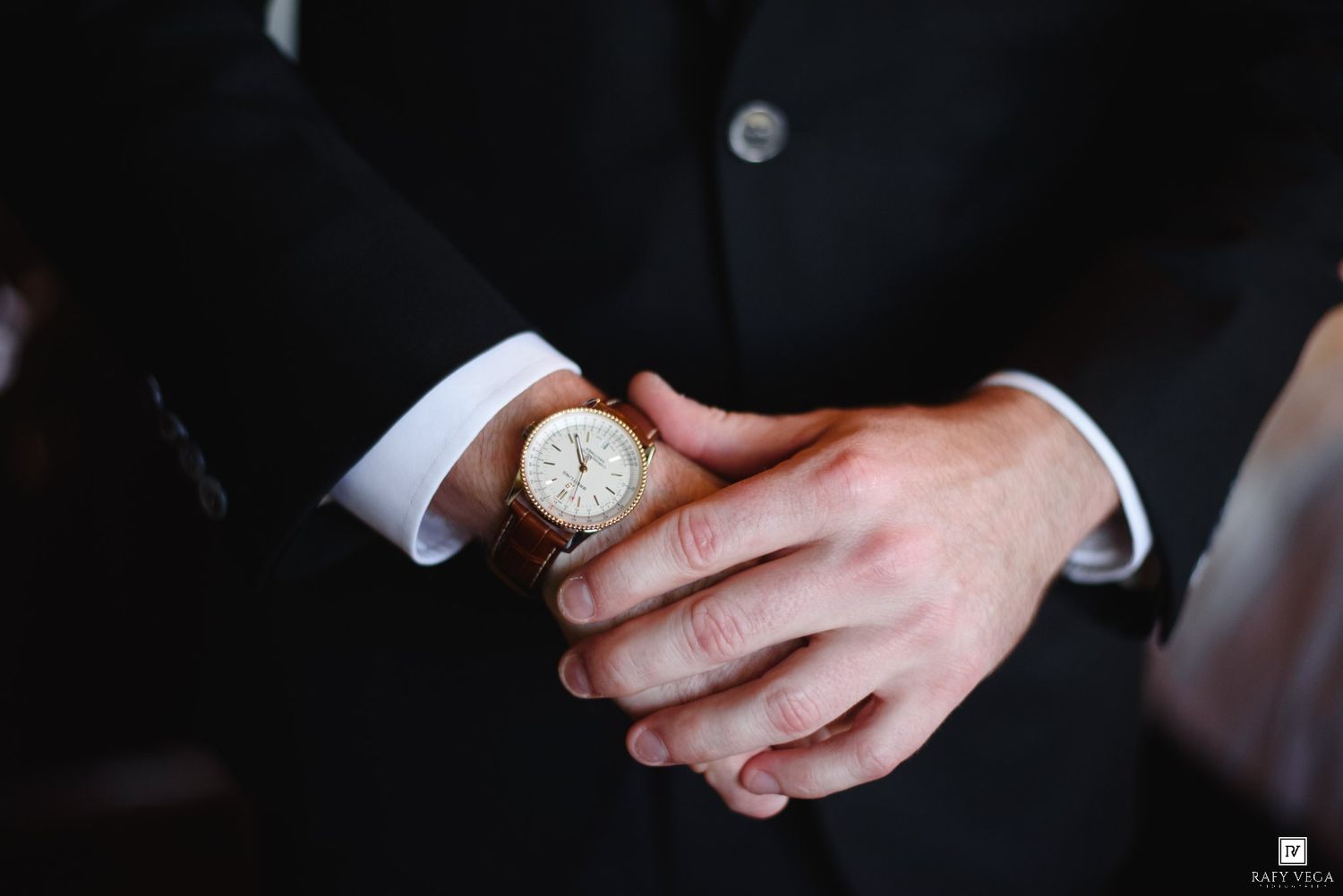 Close-up of a groom adjusting his gold watch while wearing a black suit on his wedding day.