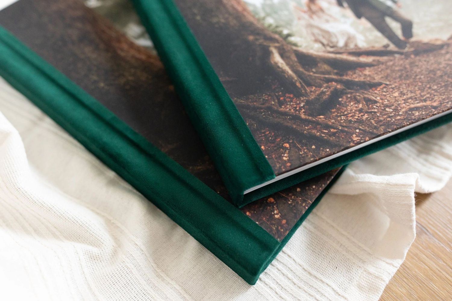 Close-up of two green velvet hardcover wedding photo albums stacked on white linen fabric.