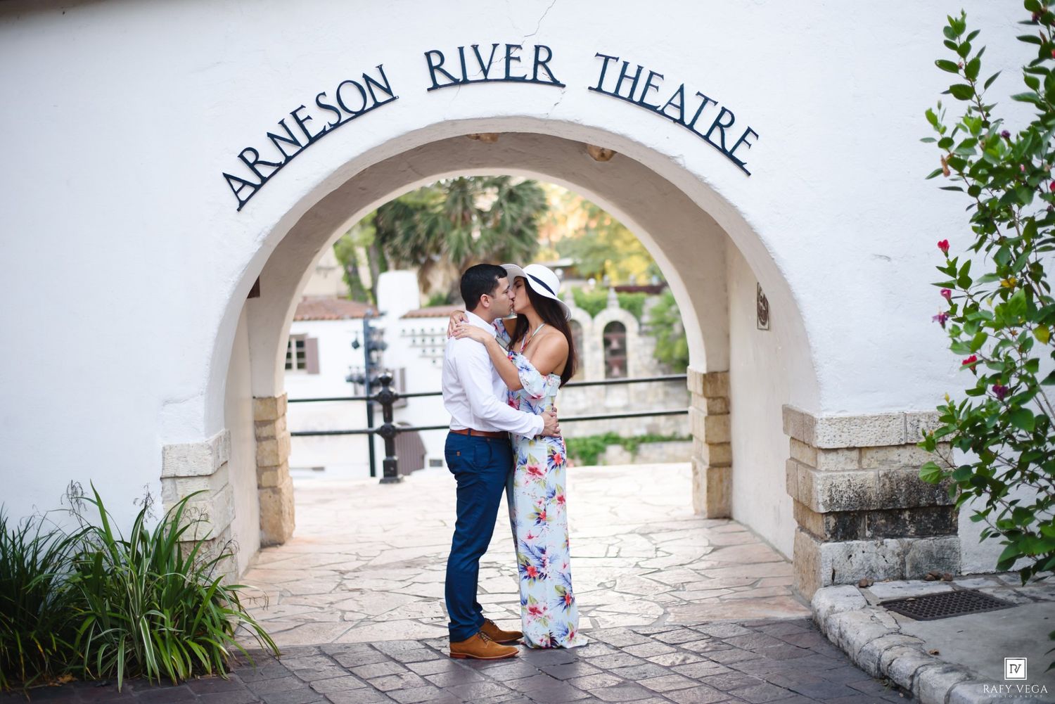 Couple sharing a romantic kiss under the Arneson River Theatre arch in San Antonio.